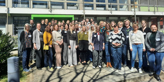Many people in colorful clothing stand in front of a building at the Technical University of Dortmund.en Universität Dortmund.